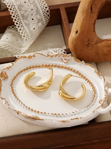 Detailed shot of irregular gold wave earrings on an elegant white vintage tray