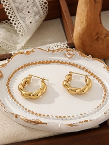 Close-up of gold twisted croissant earrings on a vintage ceramic jewelry tray