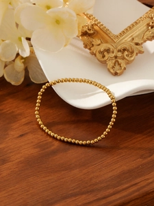 Polished gold beaded elastic bracelet resting on an elegant white ceramic display tray