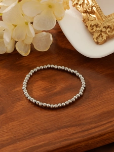 Close-up of minimalist polished silver steel beaded bracelet on a premium wooden base