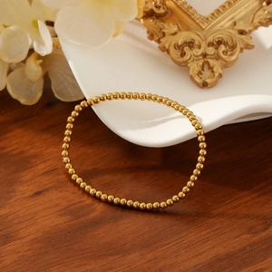 Elegant gold plated stainless steel bead bracelet displayed on a white ceramic plate