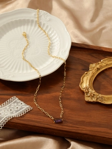 Detailed shot of a gold paperclip chain necklace with a purple rectangular gemstone