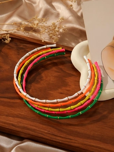 Detail view of five colorful bamboo-style headbands with gold rings in a wooden tray