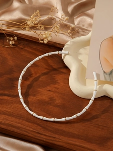 Detail view of gold-plated bamboo choker with white enamel segments on a silk background