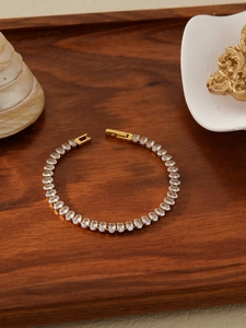 Detail of 18k gold plated tennis bracelet with clear oval-cut zircon on wood tray
