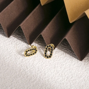 Détail de boucles d'oreilles ovales dorées avec pavage noir sur fond de texture géométrique