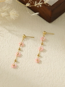 Detailed view of floral dangle earrings with pink woven petals and golden beads