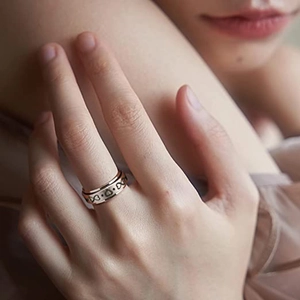 Dettaglio di anello girevole in oro rosa con cuori e simboli infinito sulle dita