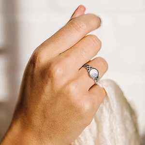Nahaufnahme eines keltischen Mondsteinrings am Finger vor weichem Strickhintergrund