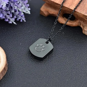 Detailansicht des schwarzen Edelstahl-Dog-Tags mit einer 3D-geprägten Pfotenabdruck-Gravur