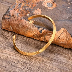 Primer plano del brazalete en C de acero inoxidable dorado con patrón grabado y textura