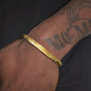 Primer plano del brazalete de acero inoxidable dorado con patrón en V en la muñeca