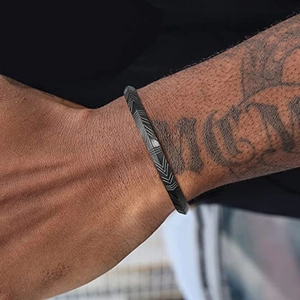 Detalle de brazalete de acero inoxidable negro mate con grabado de chevrón en la muñeca