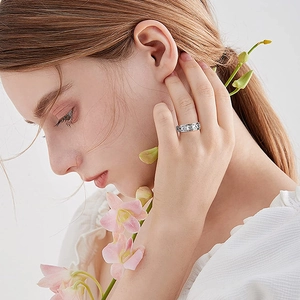 Nahaufnahme eines silbernen Herzrings mit Cut-out-Details an einem Model mit rosa Blumen