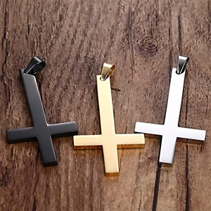 Trois pendentifs croix inversée en noir, or et argent sur fond de bois sombre