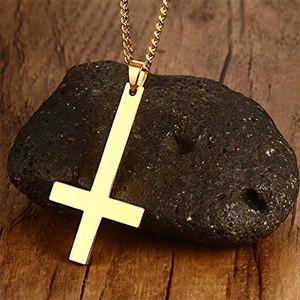 Détail macro d'un pendentif croix inversée dorée polie posé sur une pierre minérale sombre