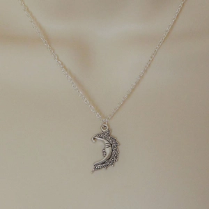 Detailed view of silver crescent moon pendant with face carving and textured finish