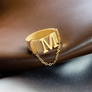 Detail of gold mesh ring featuring M initial and MOM engraving with a hanging chain