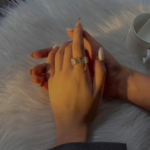 Exaggerated metal M letter ring with chain design on hand in warm sunset lighting