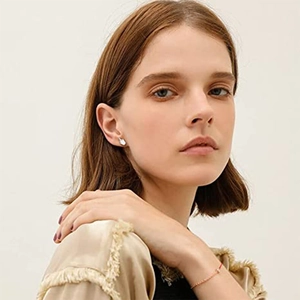 Close-up of silver swan stud earring and thin gold chain bracelet with red string detail
