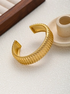 Détail montrant la texture nervurée verticale sur un large bracelet jonc ouvert doré