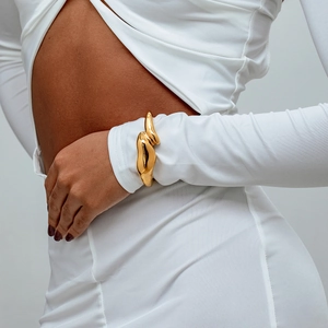 Gros plan d'un large bracelet doré aux formes organiques fluides porté sur le poignet