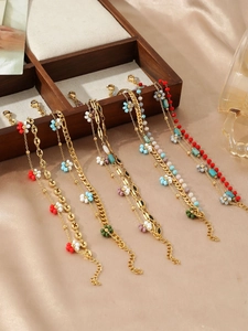 Detail of layered gold ankle bracelets with colorful beads and floral charms on wood