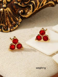 Macro detail of three red zircon stud earrings with golden base and 1g weight