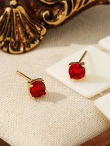 Macro shot of red round gemstone earrings with gold prong setting on vintage fabric