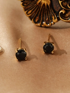 Detailed view of black zircon studs with golden four-prong setting on silk fabric