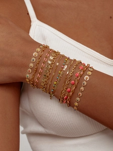 Dettaglio dei bracciali a catena d'oro boho multistrato con cuori rosa e ciondoli in smalto