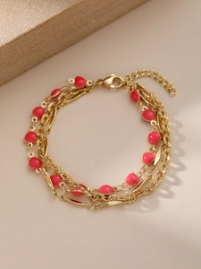 Dettaglio di un bracciale triplo strato dorato con ciondoli a cuore in smalto rosso