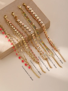 Dettaglio di catene boho dorate con cuori in smalto e dischi floreali su supporto beige