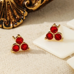 Elegant gold earrings set with three ruby-red gems on textured cream background