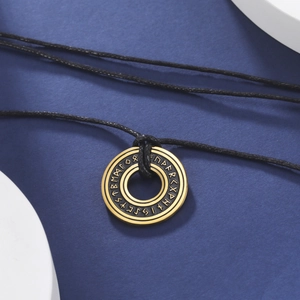 Dettaglio di pendente circolare con rune nordiche incise e finitura dorata su cordino