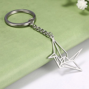 Detailed view of an origami crane stainless steel keychain on a textured surface