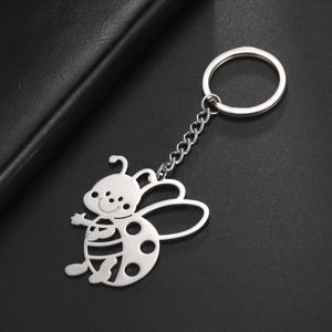 Close-up of stainless steel bee keychain with hollow cutouts on black leather background