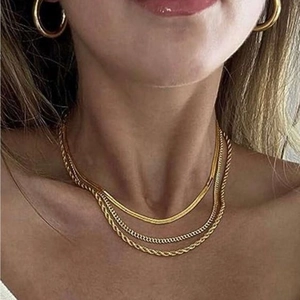 Close-up of layered golden snake and rope chain necklaces on a female model neck