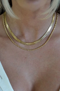 Detail of layered gold herringbone snake chain and rope chain necklace on model