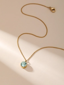 Nahaufnahme einer Goldkette mit hellgrünem Edelstein-Anhänger und Karabinerverschluss