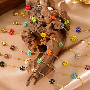 Detail bunter Perlenblumenarmbänder an Goldketten auf champagnerfarbenem Satinstoff