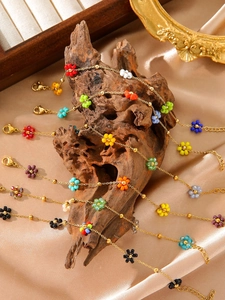 Detail bunter Perlenblumen-Armbänder mit goldener Kette auf champagnerfarbener Seide
