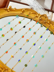Nahaufnahme bunter handgefertigter Perlenblumenketten auf einem goldenen Spiegel