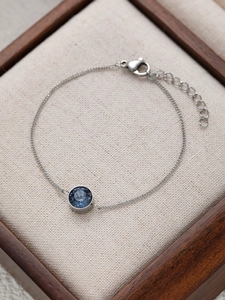 Makroaufnahme eines silbernen Armbands mit facettiertem blauem Edelstein in einer Geschenkbox