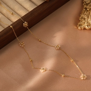 Gros plan du collier doré avec fleurs crème mates et petites perles en métal