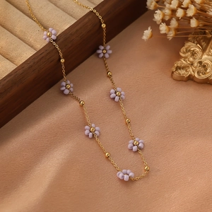 Détail d'un collier chaîne dorée avec fleurs en perles mauves sur une boîte élégante