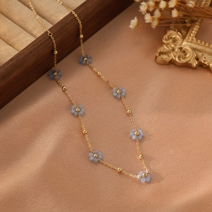 Détail d'un collier doré orné de fleurs bleu clair et de perles dorées sur fond de satin