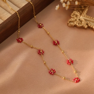 Détail d'un collier doré élégant avec petites fleurs rouges en perles et billes d'or