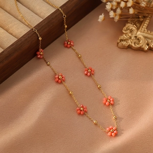 Détail d'un collier doré orné de fleurs orange sur un fond élégant en soie beige