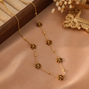 Détail du collier à fleurs dorées avec perles facettées sur fond de soie orange et satin
